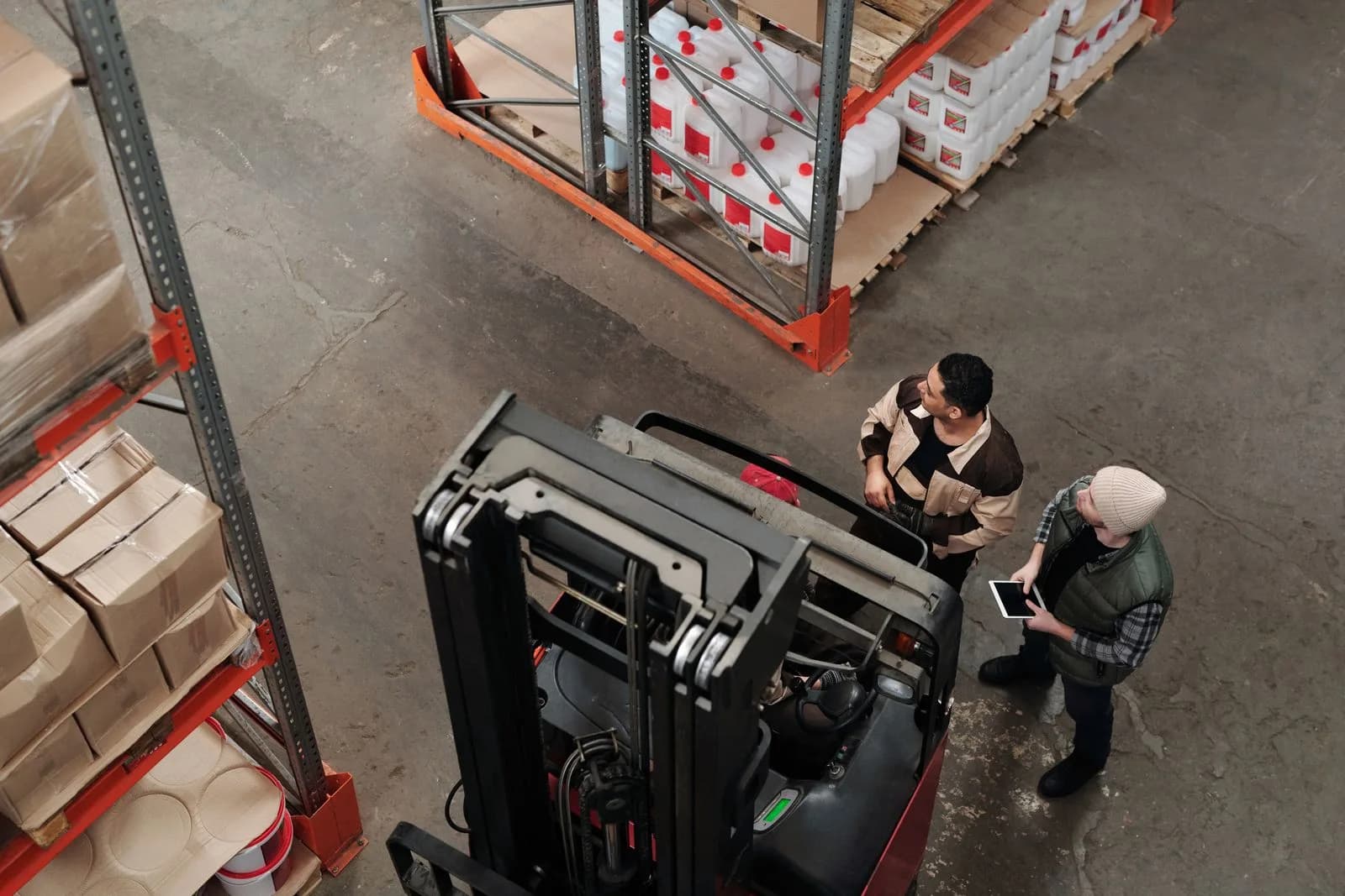 Warehouse team discussing logistics near a forklift, illustrative campaign image